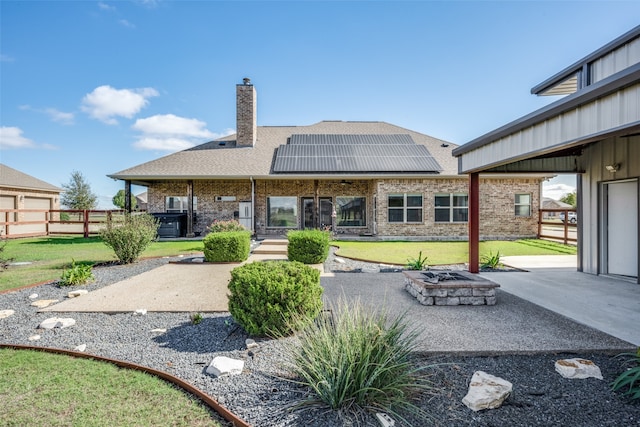 rear view of house with a yard, solar panels, a patio, and a fire pit