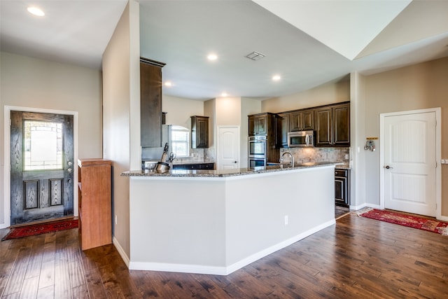 kitchen featuring kitchen peninsula, appliances with stainless steel finishes, tasteful backsplash, light stone countertops, and dark hardwood / wood-style flooring