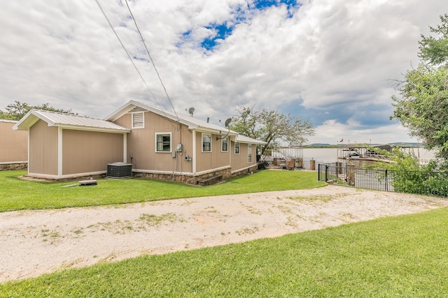 rear view of property with central air condition unit, a lawn, and a water view