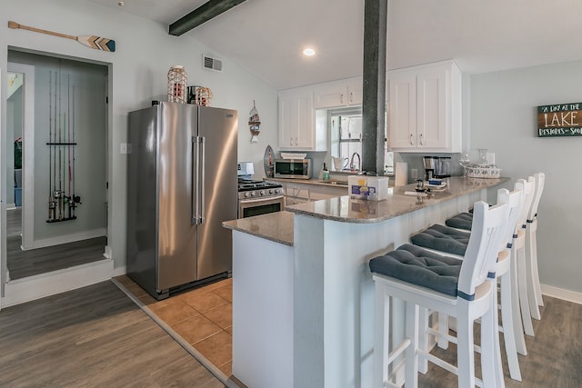 kitchen featuring white cabinets, hardwood / wood-style floors, stainless steel appliances, and vaulted ceiling with beams