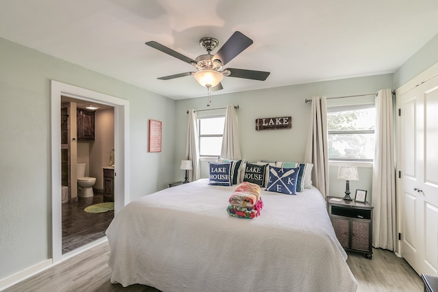 bedroom with ensuite bathroom, ceiling fan, multiple windows, and light wood-type flooring