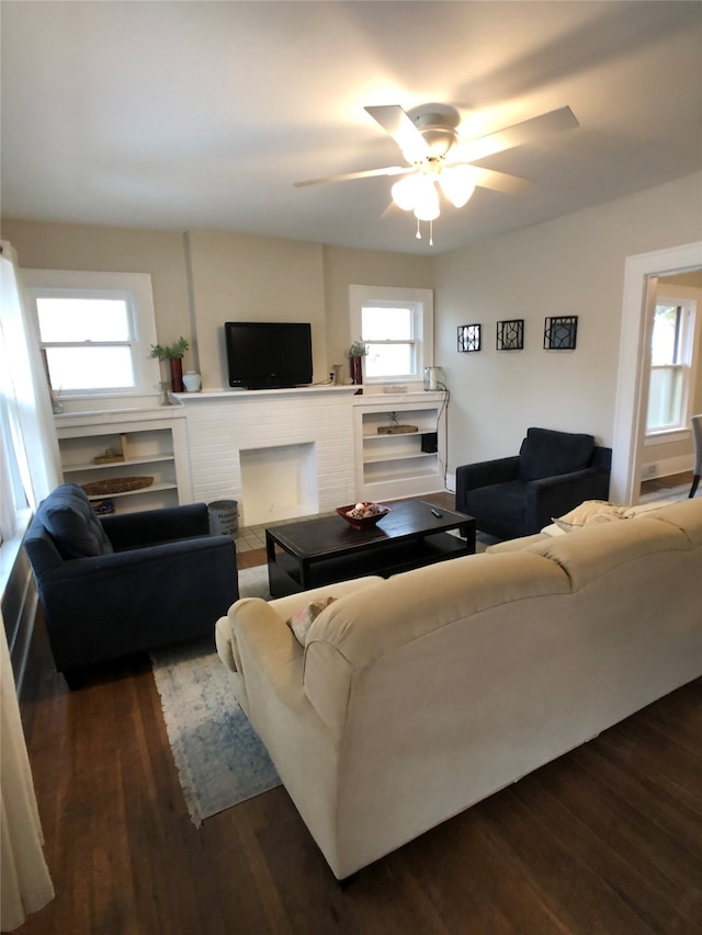 living room featuring a brick fireplace, dark wood-type flooring, a healthy amount of sunlight, and ceiling fan