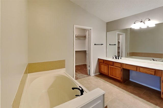 bathroom featuring a bath, vanity, a textured ceiling, tile patterned flooring, and lofted ceiling