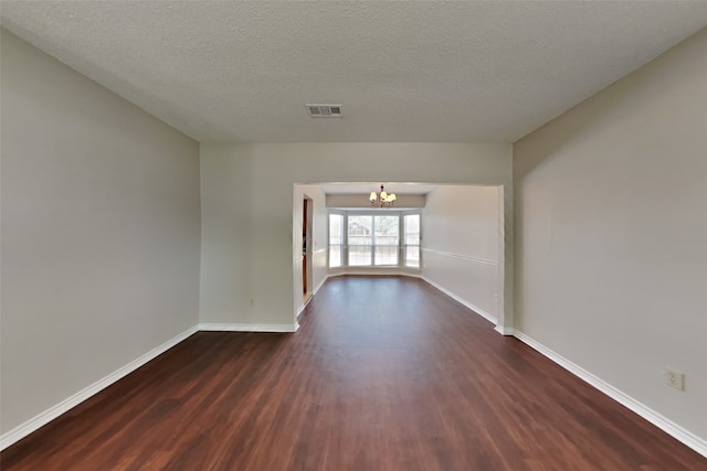 spare room featuring a textured ceiling, a notable chandelier, and dark hardwood / wood-style floors