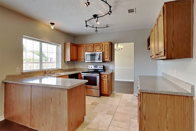 kitchen with sink, track lighting, kitchen peninsula, appliances with stainless steel finishes, and a textured ceiling