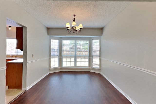 unfurnished dining area with a wealth of natural light, a chandelier, a textured ceiling, and dark hardwood / wood-style flooring