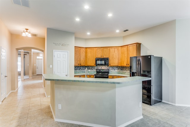 kitchen featuring backsplash, a kitchen island with sink, sink, black appliances, and light tile patterned floors