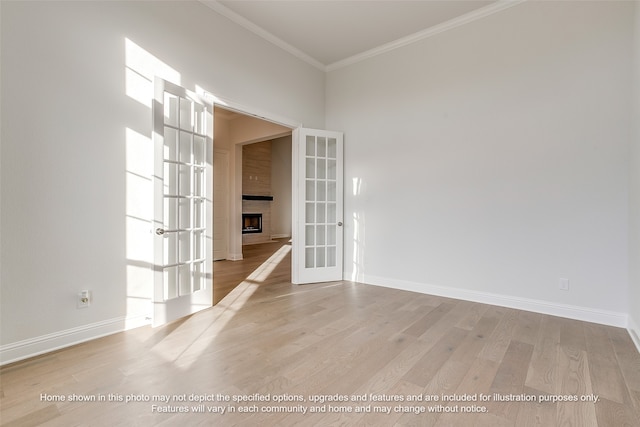 spare room with light wood-style floors, french doors, a large fireplace, and ornamental molding