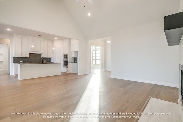 unfurnished living room with high vaulted ceiling, baseboards, a sink, and light wood finished floors