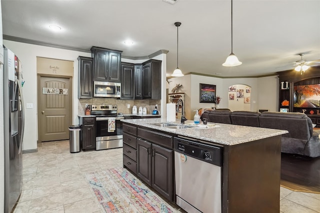 kitchen featuring backsplash, ornamental molding, stainless steel appliances, decorative light fixtures, and an island with sink