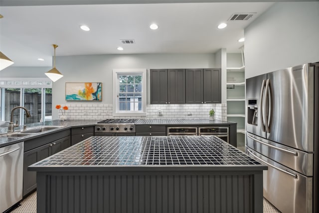 kitchen featuring tasteful backsplash, stainless steel appliances, a kitchen island, pendant lighting, and sink