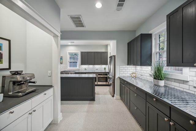 kitchen featuring white cabinetry, backsplash, appliances with stainless steel finishes, and light tile patterned floors