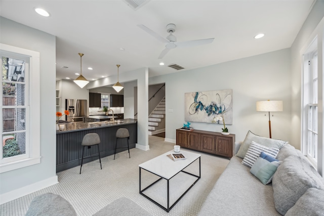 carpeted living room featuring ceiling fan and sink