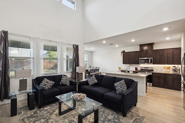 living room with a towering ceiling, light hardwood / wood-style floors, and sink