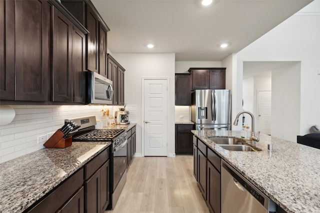 kitchen with stainless steel appliances, sink, light stone counters, backsplash, and light hardwood / wood-style flooring