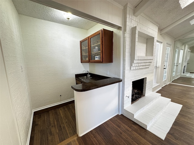 kitchen featuring sink, a brick fireplace, dark hardwood / wood-style floors, a textured ceiling, and beam ceiling