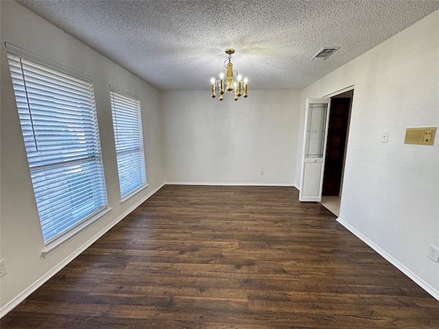 empty room with a textured ceiling, dark wood-type flooring, and a notable chandelier