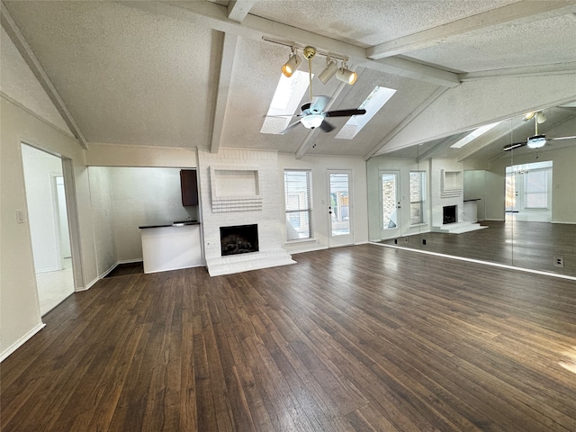 unfurnished living room featuring vaulted ceiling with skylight, a textured ceiling, ceiling fan, a fireplace, and dark hardwood / wood-style floors