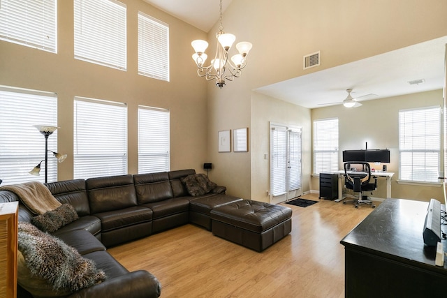 living room featuring ceiling fan with notable chandelier, a high ceiling, and light wood-type flooring