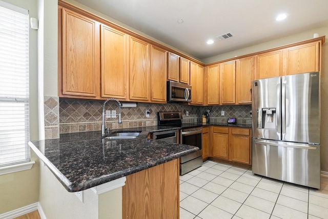 kitchen featuring light tile patterned flooring, sink, dark stone countertops, appliances with stainless steel finishes, and kitchen peninsula