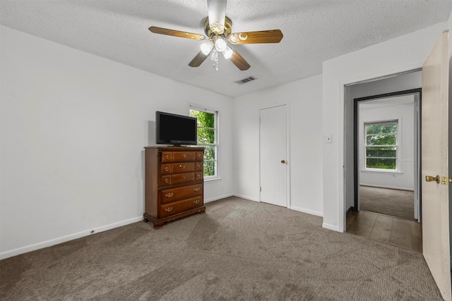 unfurnished bedroom with ceiling fan, a textured ceiling, a closet, and dark carpet