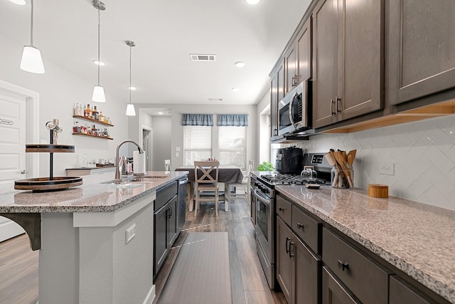 kitchen with appliances with stainless steel finishes, light hardwood / wood-style floors, pendant lighting, light stone counters, and sink