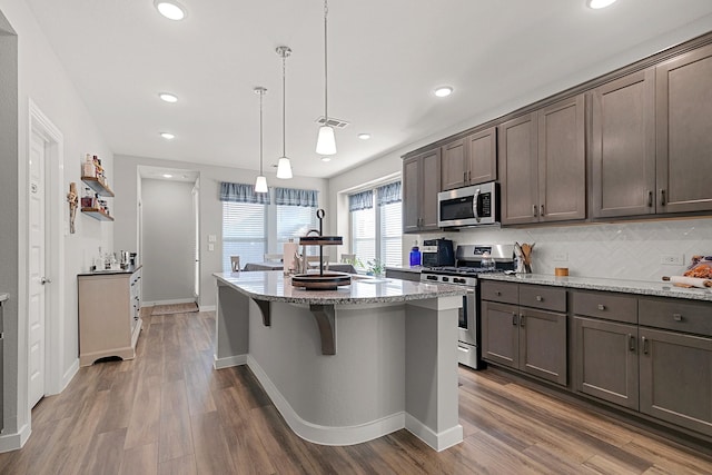 kitchen with a kitchen island, wood-type flooring, hanging light fixtures, stainless steel appliances, and light stone countertops