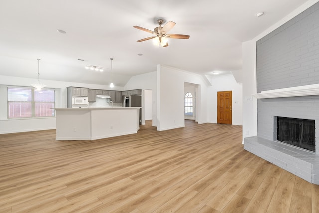 unfurnished living room with a fireplace, vaulted ceiling, ceiling fan, and light hardwood / wood-style flooring