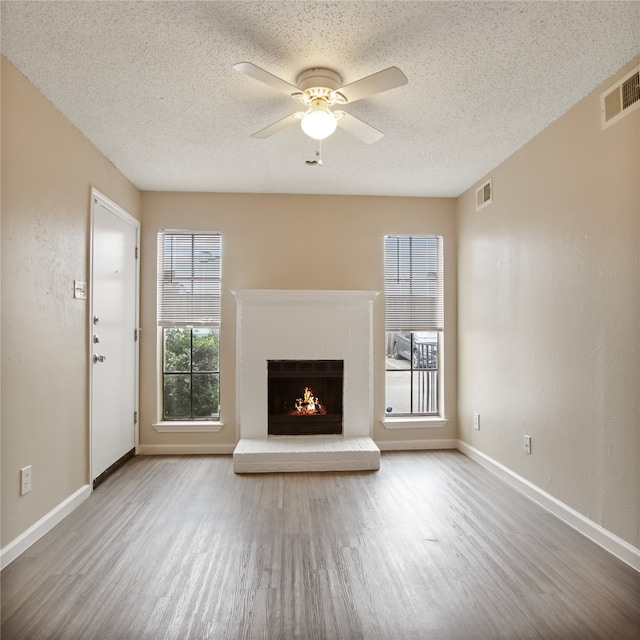 unfurnished living room featuring a brick fireplace, wood-type flooring, a textured ceiling, and ceiling fan