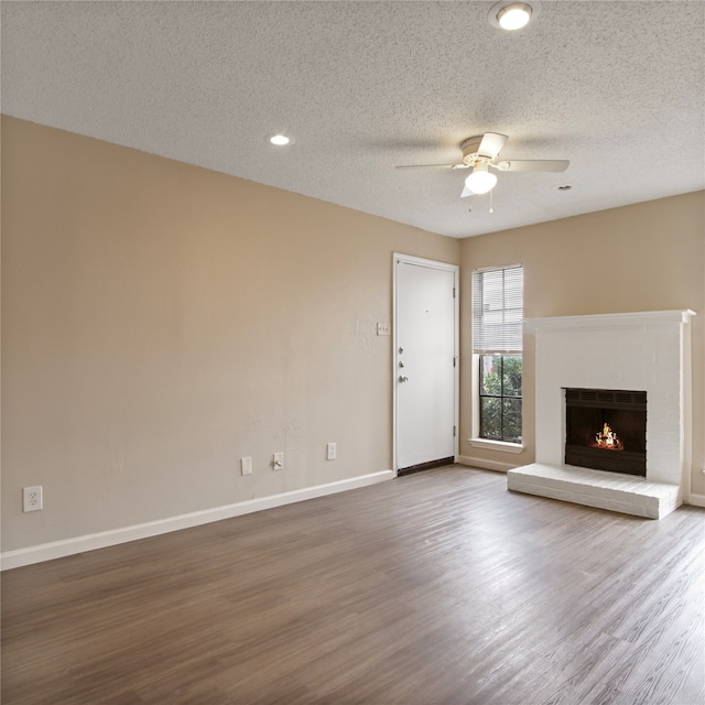 unfurnished living room featuring a fireplace, wood-type flooring, a textured ceiling, and ceiling fan