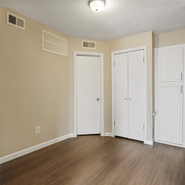 unfurnished bedroom with dark wood-type flooring, a textured ceiling, and two closets