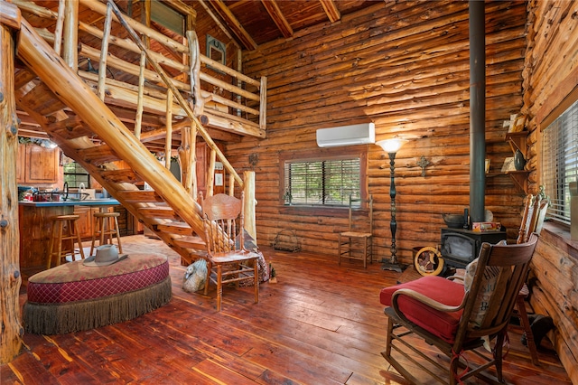 sitting room featuring beamed ceiling, wood-type flooring, a wood stove, log walls, and an AC wall unit