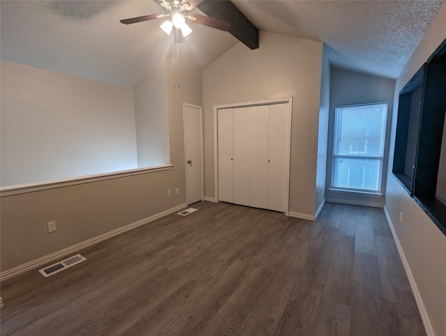 unfurnished bedroom featuring ceiling fan, a textured ceiling, dark wood-type flooring, a closet, and lofted ceiling with beams