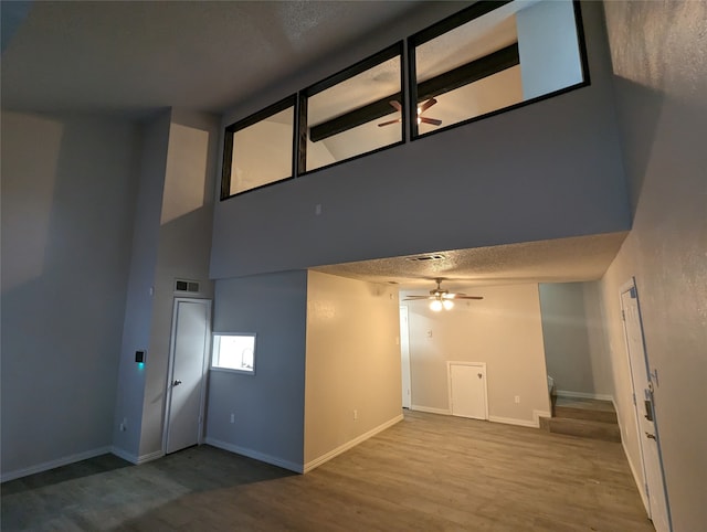 interior space featuring a textured ceiling, hardwood / wood-style floors, ceiling fan, and a towering ceiling