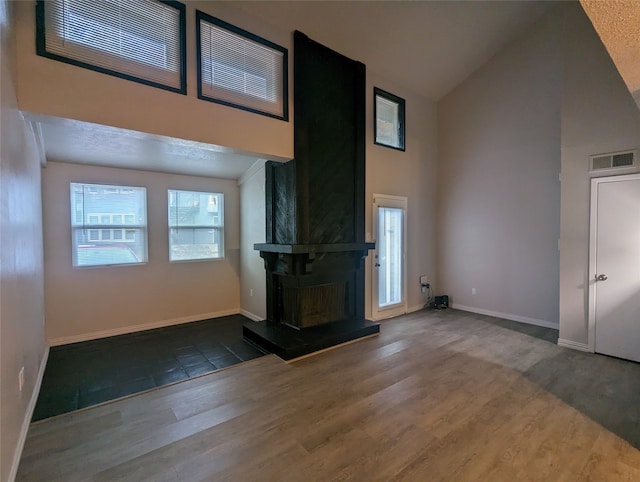 unfurnished living room with dark wood-type flooring, high vaulted ceiling, a textured ceiling, and a fireplace