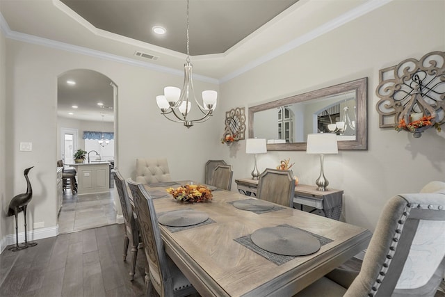 dining area with dark wood-type flooring, a chandelier, a raised ceiling, and crown molding