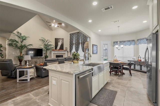 kitchen featuring stainless steel appliances, a center island with sink, light stone counters, decorative light fixtures, and white cabinets