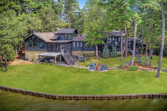 rear view of house featuring a sunroom, a deck with water view, a lawn, and an outdoor fire pit