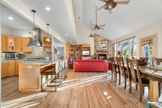 interior space with a breakfast bar, high vaulted ceiling, wall chimney exhaust hood, a fireplace, and stainless steel appliances