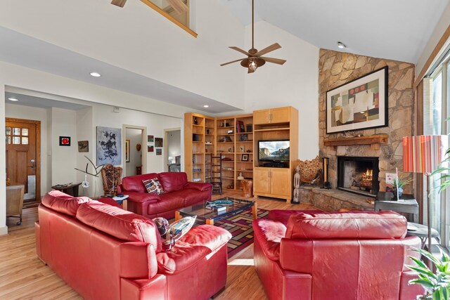 living room featuring ceiling fan, light wood-type flooring, a fireplace, and high vaulted ceiling