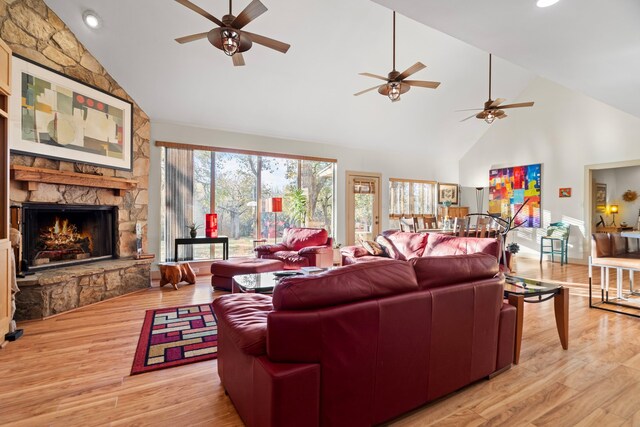 living room featuring a fireplace, light hardwood / wood-style floors, high vaulted ceiling, and ceiling fan