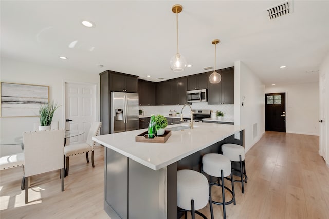 kitchen with stainless steel appliances, backsplash, decorative light fixtures, dark brown cabinets, and light hardwood / wood-style floors