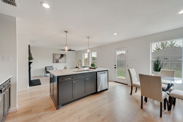 kitchen featuring light wood-type flooring, decorative light fixtures, sink, an island with sink, and stainless steel dishwasher