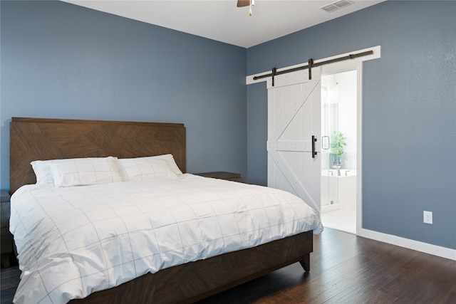 bedroom with a barn door, ensuite bathroom, dark hardwood / wood-style floors, and ceiling fan