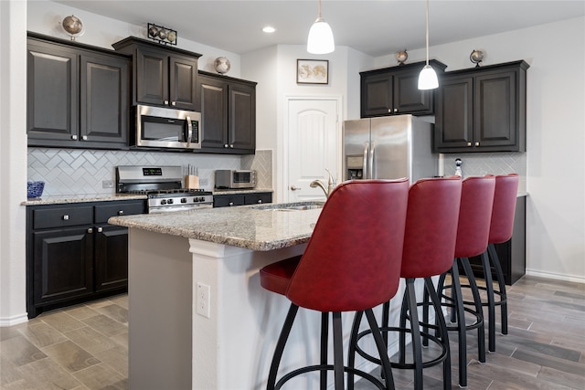 kitchen with sink, stainless steel appliances, a kitchen breakfast bar, pendant lighting, and a center island with sink