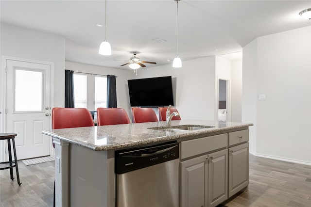 kitchen featuring pendant lighting, a center island with sink, stainless steel dishwasher, and light hardwood / wood-style flooring