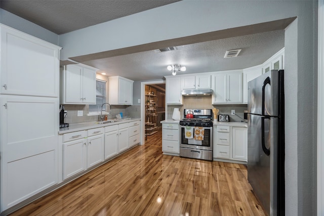 kitchen featuring black fridge, white cabinetry, stainless steel gas range, decorative backsplash, and light hardwood / wood-style floors