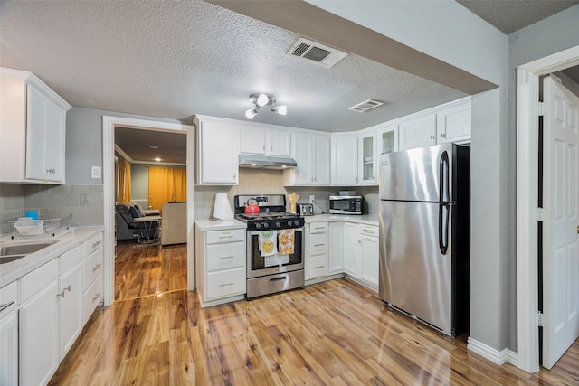 kitchen with white cabinets, light wood-type flooring, appliances with stainless steel finishes, and tasteful backsplash