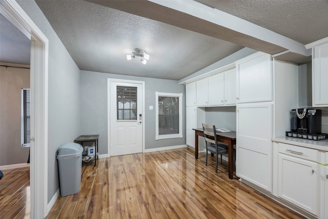 interior space featuring white cabinetry, light hardwood / wood-style flooring, and a textured ceiling