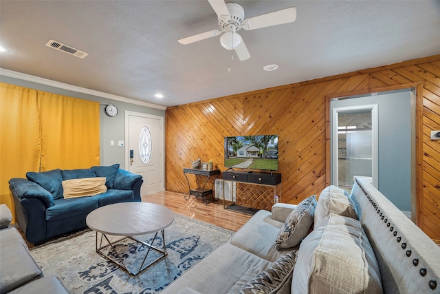 living room with ornamental molding, light wood-type flooring, wood walls, and ceiling fan